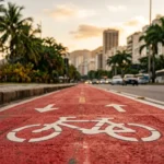 Ciclovia pintada de vermelho ao longo de uma avenida urbana brasileira, vista rente ao asfalto