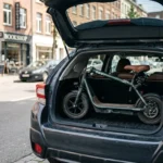 Scooter elétrica dobrada ao lado do porta-malas aberto de um carro